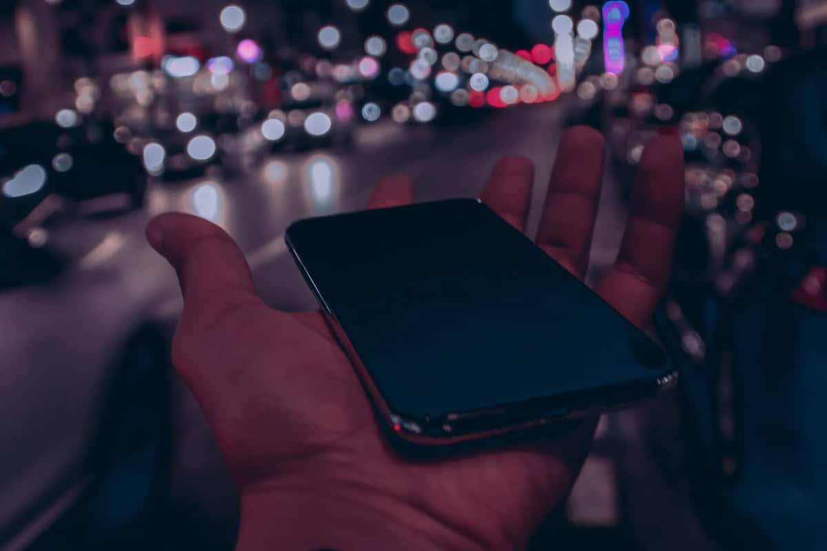 Smartphone tenu en main dans une rue de nuit, illustrant la connexion mobile en voyage